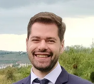 Mario Molnar smiling outdoors, green hills behind him